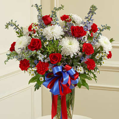 Red roses and white chrysanthemums in a glass vase with a red and blue ribbon