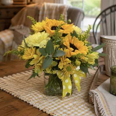 Yellow sunflower and daisy bouquet in a glass vase with a polka-dot ribbon