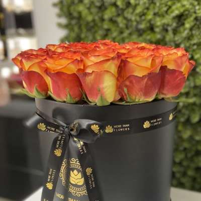 Round black hatbox filled with orange and yellow roses and tied with a black ribbon.