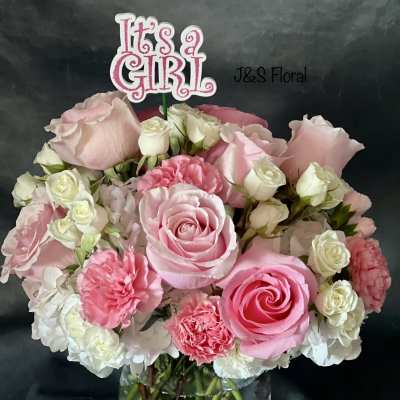Pink and white rose bouquet in a clear vase with an "It's a Girl" topper.