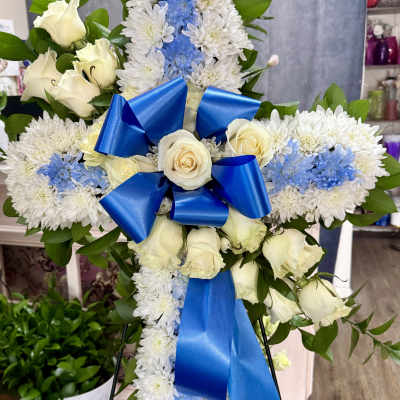 White floral standing cross with blue ribbon and roses