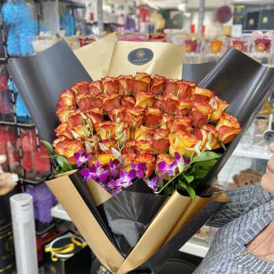 Large bouquet of orange roses with purple orchids wrapped in black and gold paper
