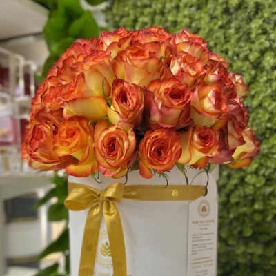 Round hatbox of orange and yellow roses tied with a gold ribbon