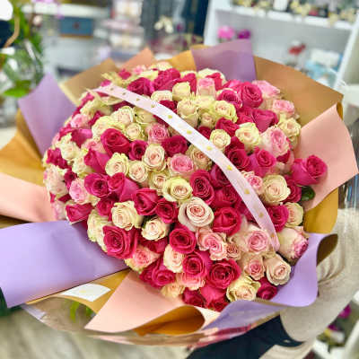 Large round bouquet of hot pink, light pink, and cream roses wrapped in multicolored paper.