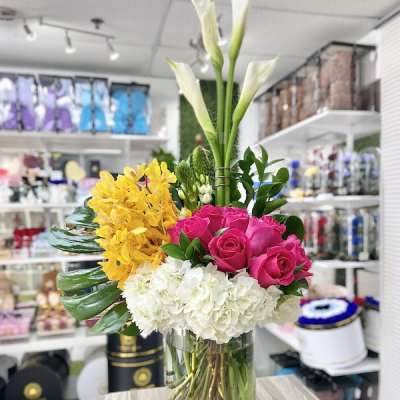 Tall arrangement of white calla lilies, yellow orchids, hot pink roses, and white hydrangeas in a glass vase