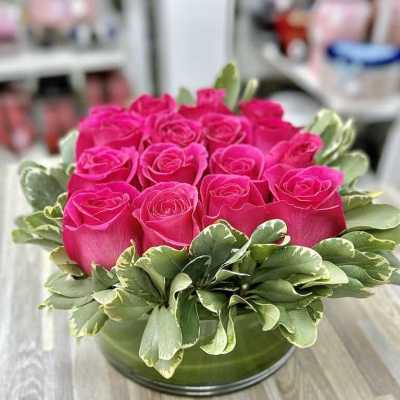 Round arrangement of hot pink roses with a ring of variegated leaves in a low glass vase
