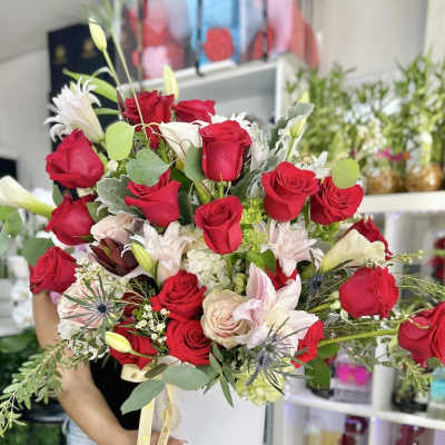 Large arrangement of red roses with pale pink and white lilies in a round white hatbox container