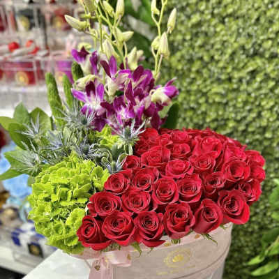 Round hatbox arrangement with red roses, green hydrangeas, and purple orchids