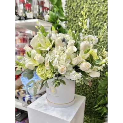 White and cream flower arrangement with roses, lilies, and hydrangeas in a round white hatbox container