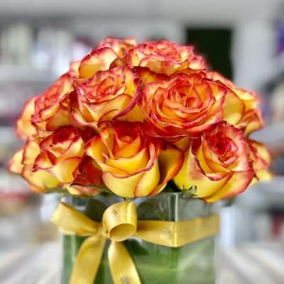 Compact bouquet of yellow roses with red edges in a square glass vase tied with a yellow ribbon