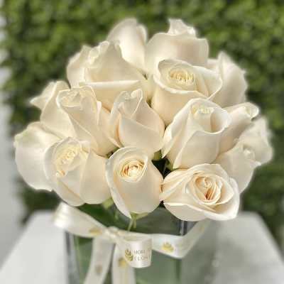 Compact arrangement of cream roses in a clear glass cube vase with a white ribbon bow