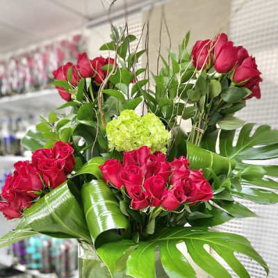Tall arrangement of red roses with large tropical leaves in a square glass vase