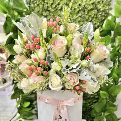 Round hatbox arrangement of pale pink and white roses with pink berries and foliage, tied with a pink ribbon.