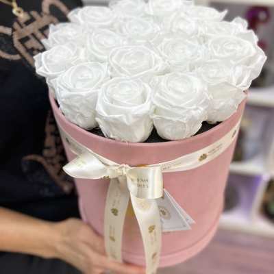Round pink hatbox packed with white roses and tied with an ivory ribbon.