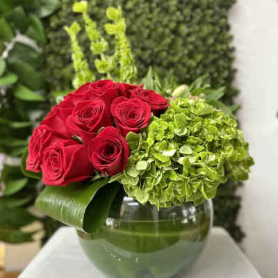Low arrangement of red roses and green hydrangeas in a round glass vase