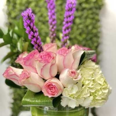 Low arrangement of pink roses, white hydrangea and tall purple spikes in a round glass bowl vase