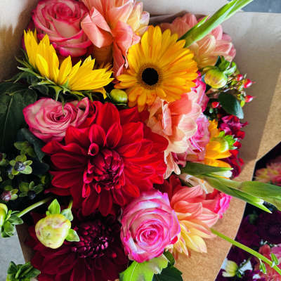 Mixed bouquet with roses, dahlias, and yellow daisies in brown paper