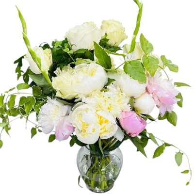 White and blush peony and rose arrangement with trailing vines in a clear glass vase
