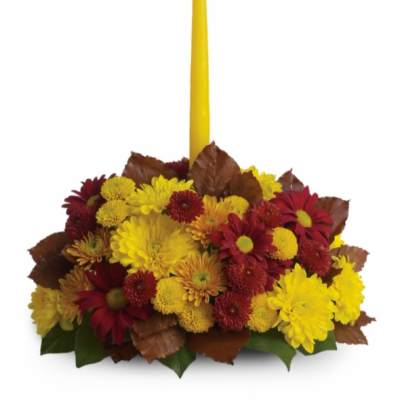 Yellow taper candle in a low arrangement of red and yellow chrysanthemums
