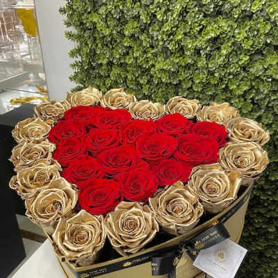 Heart-shaped gold box filled with red and gold roses and tied with a black ribbon