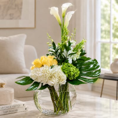 White calla lilies, yellow roses, and green hydrangeas in a glass vase.