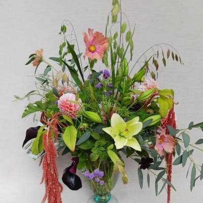 Tall garden-style arrangement with pink dahlias, green lily, dark calla lilies in a clear glass vase