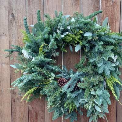 Evergreen wreath with pinecones and mixed foliage hanging on a wooden fence