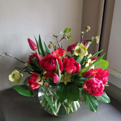 Low round arrangement of red ranunculus and tulips with pale yellow blooms in a clear glass bowl vase.