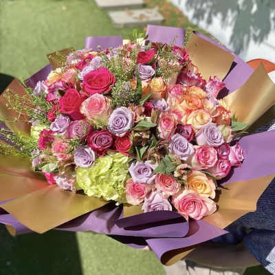 Large hand-tied bouquet of pink, lavender, and peach roses wrapped in purple and gold paper