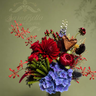 Red and blue floral arrangement in a clear glass vase with a bronze heart accent