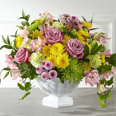 Mixed bouquet of pink roses, yellow blooms, and green flowers in a white vase