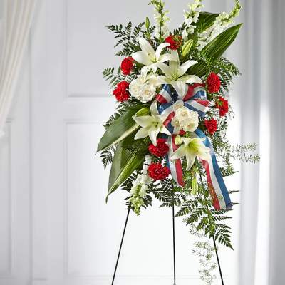 Standing floral spray with white lilies, red carnations, and a patriotic ribbon