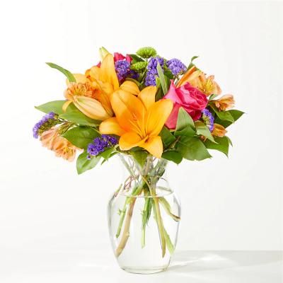 Bright mixed bouquet of lilies, roses, and purple filler flowers in a clear glass vase
