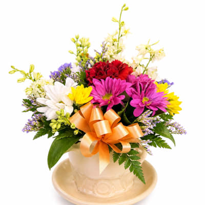 Colorful mixed bouquet in a cream vase with an orange ribbon