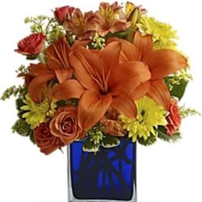 Orange lilies and mixed flowers in a blue glass vase