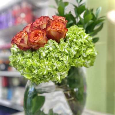 Round glass vase with orange roses and bright green hydrangea blooms