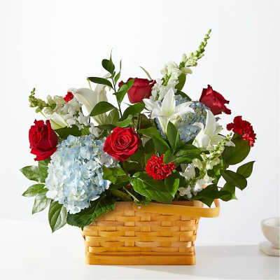 Basket arrangement of red roses, white lilies, and blue hydrangeas