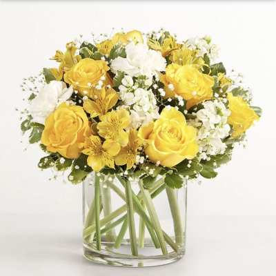 Yellow roses and white flowers arranged in a clear glass vase.