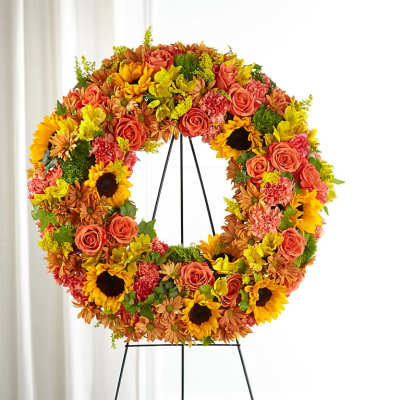 Circular floral wreath with roses, sunflowers, and mums on a black stand