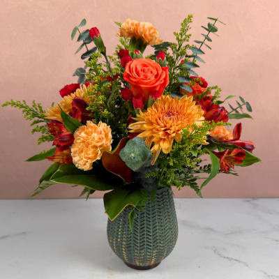 Orange and red mixed flower arrangement in a green vase