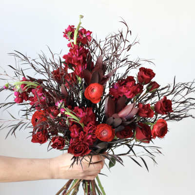 Handheld bouquet of red roses and dark foliage