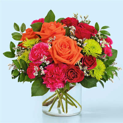 Mixed bouquet of orange, red, and pink flowers in a clear glass vase