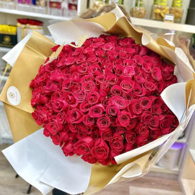 Large bouquet of hot pink roses wrapped in white and gold paper in a flower shop