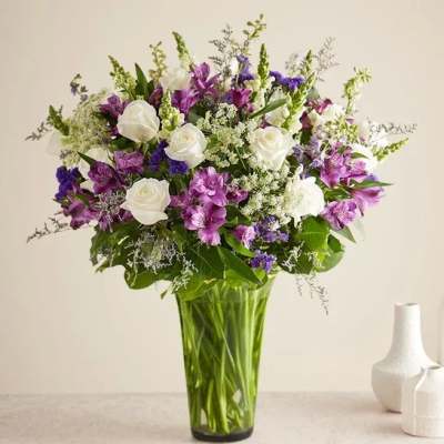 White roses and purple flowers in a tall glass vase