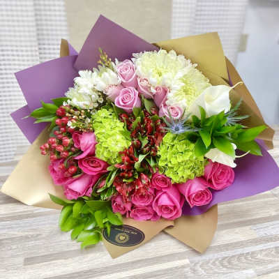 Hand-tied bouquet with pink roses, green hydrangeas, white chrysanthemums and red blooms in purple and gold wrap