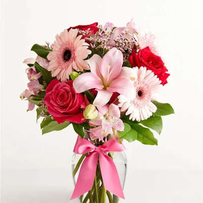 Pink and red mixed bouquet in a clear glass vase with a pink ribbon