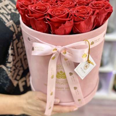 Round box of red roses in a pink hatbox with ribbon and tag