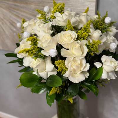 White roses arranged in a glass vase with yellow filler flowers