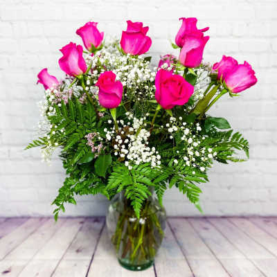 Pink roses arranged in a glass vase with baby's breath and fern