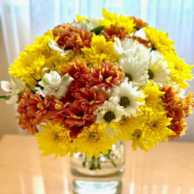 Bouquet of yellow, white, and orange daisies in a clear glass vase